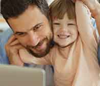 Smiling father and young daughter sharing laptop, laughing together in cozy home setting