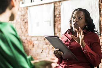 Woman holding tablet gesturing while speaking to colleague in casual meeting room