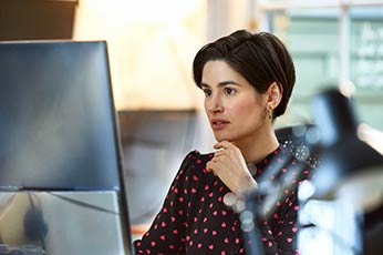 Young woman leaning on hand, intently reading computer screen in bright office