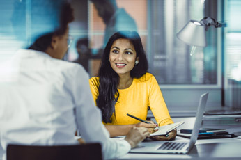 Woman in yellow sweater smiling and taking notes during meeting in modern office