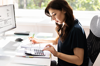 Woman calculating finances with calculator and notes at bright office desk