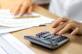 Person pressing calculator keys while reviewing financial documents on desk