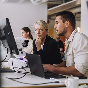 Woman and man reviewing project on laptop and monitor in modern open office
