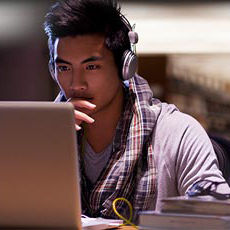 College student wearing headphones studying intently at laptop in library late night