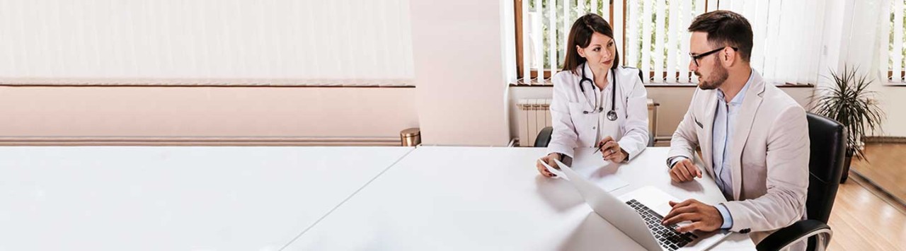 Female doctor reviewing medical records with male patient using laptop at consultation desk