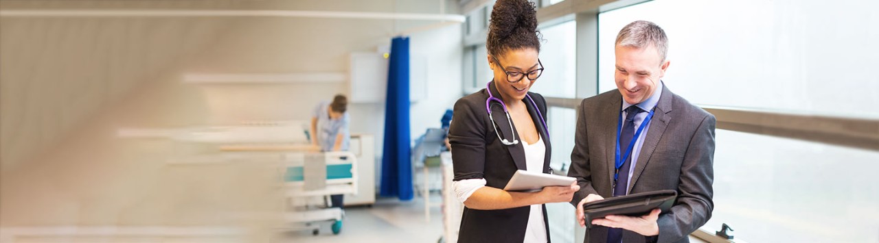 Two healthcare professionals compare tablets while standing in a bright hospital corridor