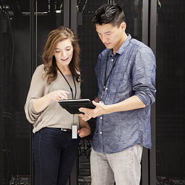 Two technicians reviewing a tablet in a server room