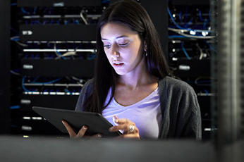 IT technician checking tablet while monitoring network servers in server racks