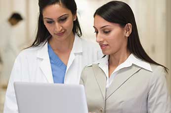 Doctor and colleague reviewing patient information on laptop in hospital corridor