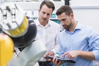 Two engineers inspecting a collaborative robot arm while reviewing tablet data in a lab