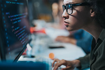 Software developer intently reviewing code on a monitor in team workspace