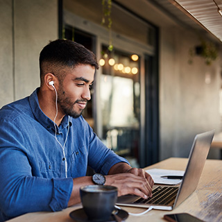An adult learner smiles as he completes online coursework on a laptop while studying from home.