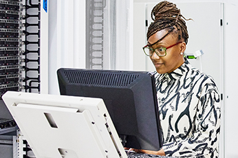 IT technician analyzing server metrics on dual monitors inside a data center rack room