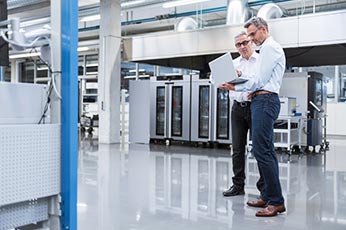 Two engineers reviewing laptop showing production data in modern manufacturing facility