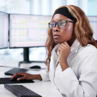 Woman with glasses reviewing medical billing and coding information on her computer monitors.