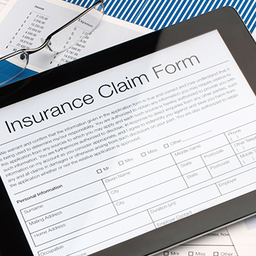Tablet displaying "Insurance Claim Form" with glasses and financial papers