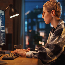 Developer typing code on multiple monitors in dimly lit home office late night