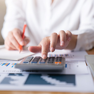 hand using a calculator on top of papers with data and graphs