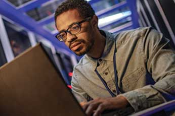Engineer concentrating on laptop amid server racks with blue lighting