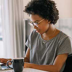 A woman wearing glasses sitting in front of a window at a desk and using a laptop.