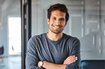 Smiling man cross-armed standing in modern office with glass walls