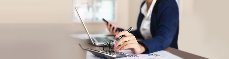 Person using calculator and smartphone while reviewing financial charts on desk