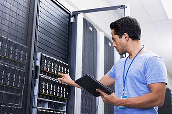 IT technician checks hard drive bays in server rack, holding tablet