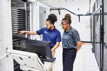 Two technicians inspecting server rack while consulting workstation in data center