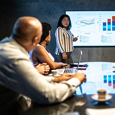 Woman presenting sales charts on screen to colleagues in conference room