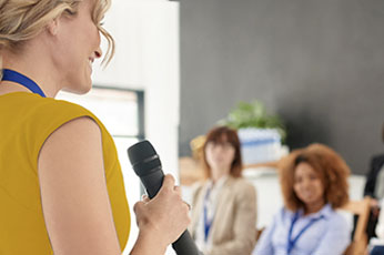 Woman speaking into microphone addressing attentive coworkers in meeting room