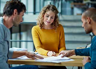 Woman in mustard sweater reviewing documents with two colleagues at modern office table