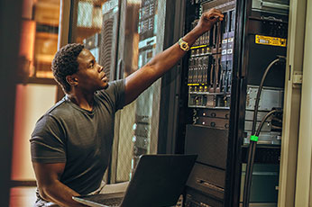 IT technician configuring rack-mounted servers in a data center with laptop