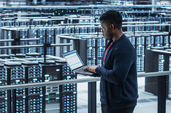 IT engineer checking laptop while monitoring server racks in data center