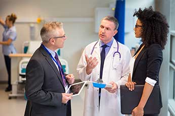 Doctor explains patient chart to two professionals in hospital corridor