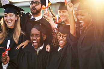 Diverse group of graduates cheering, tossing caps and holding diplomas outdoors