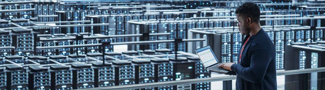Engineer inspecting laptop while monitoring rows of server racks in data center