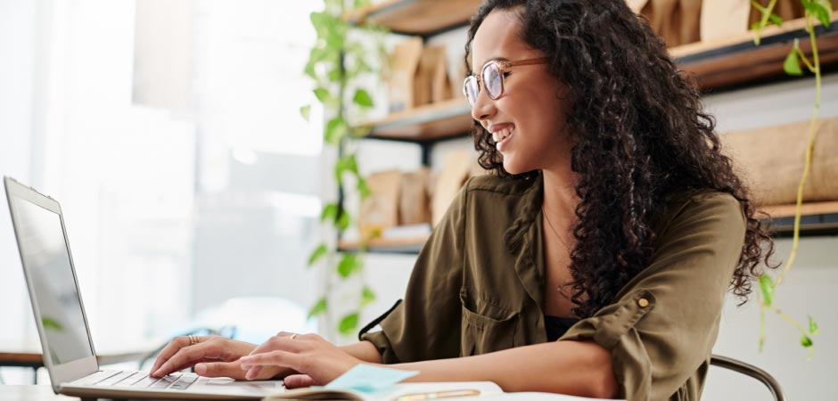 Young woman typing on laptop and smiling in cozy café workspace